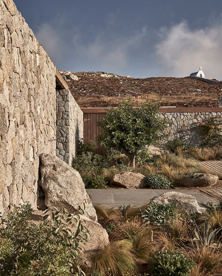 Lateral de exterior de vivienda con muros de piedra y monte con iglesia en la cima