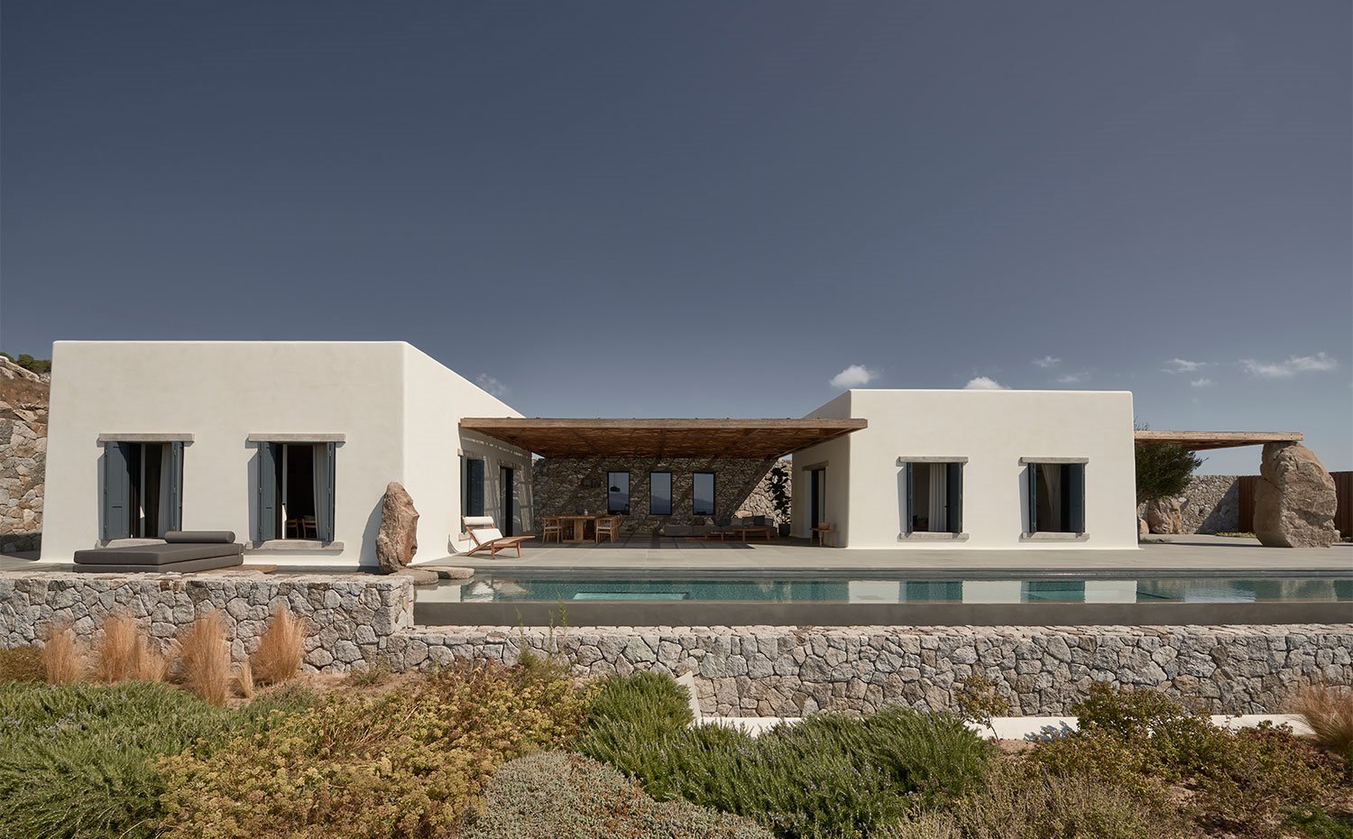 Piscina frente a vivienda con muerete de piedra, tumbonas y terraza exterior cubierta