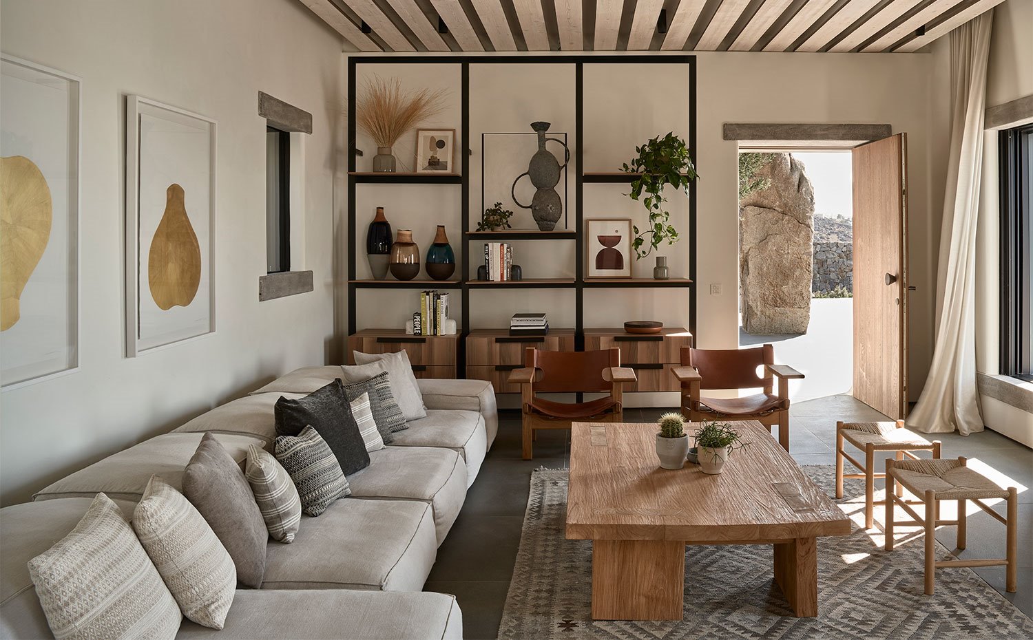Salón con sofá en gris, mesa de centro de madera y butacas de madera y piel, estantería de estructura metálica y cajones de madera