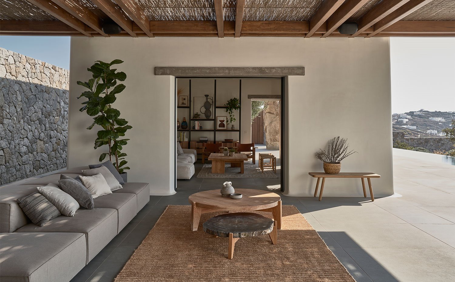 Salón exteiror con sofá en gris y mesas de madera sobre alfombra de fibras naturales