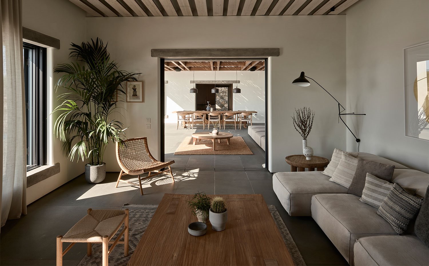 Salón interior abierto hacia el porche exterior, butaca de formas curvas de fibras naturales y gran aplique junto a sofá
