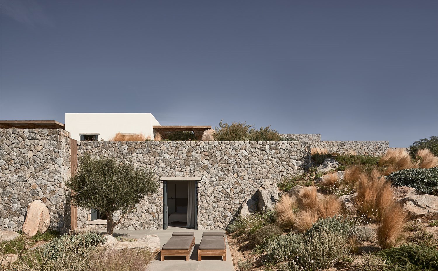 tumbonas junto a fachada de piedra de la casa que se abre al exterior 
