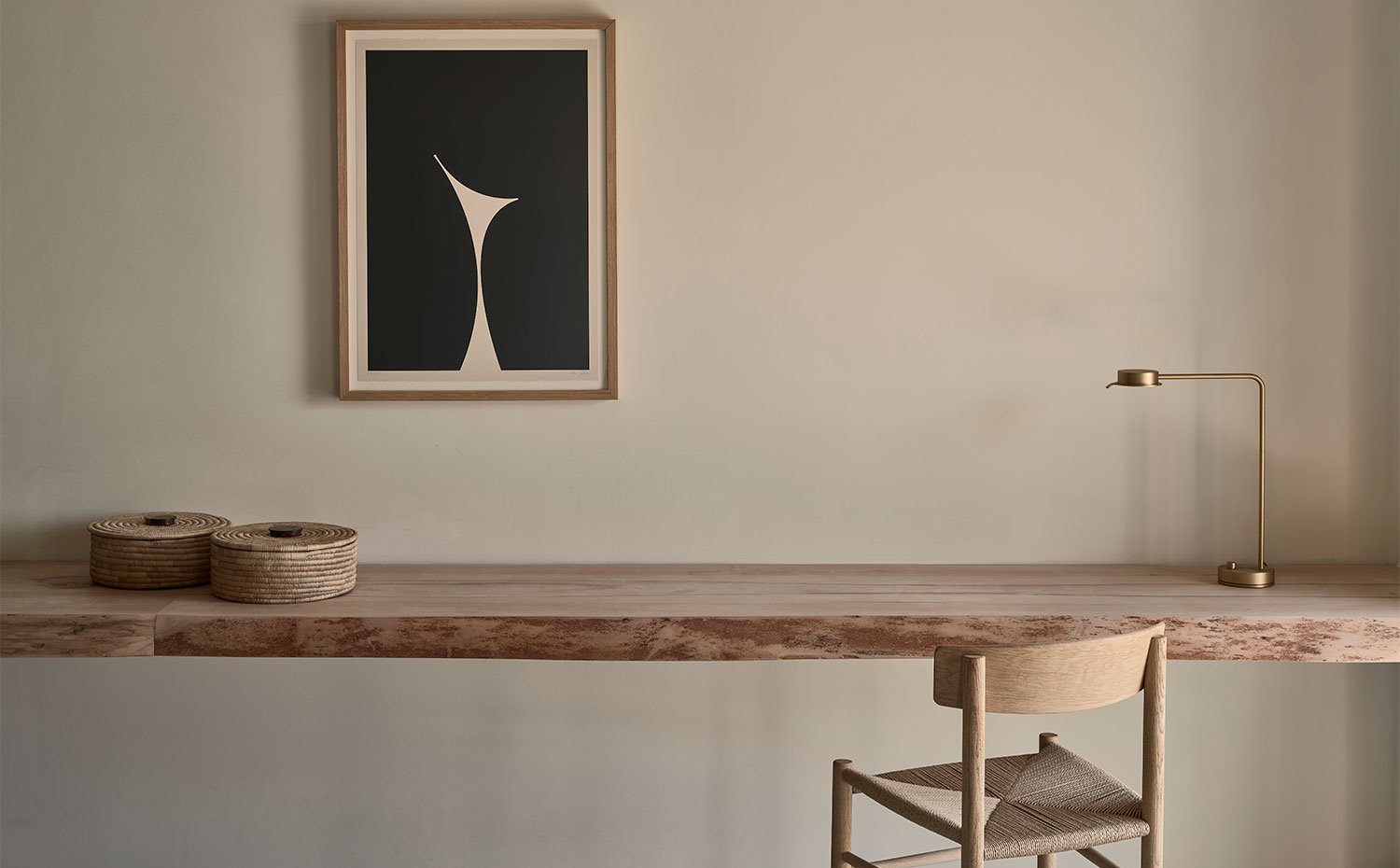 Zona de trabajo con balda de madera de pared a pared, luminaria de sobremesa en acabado latón y silla de madera 
