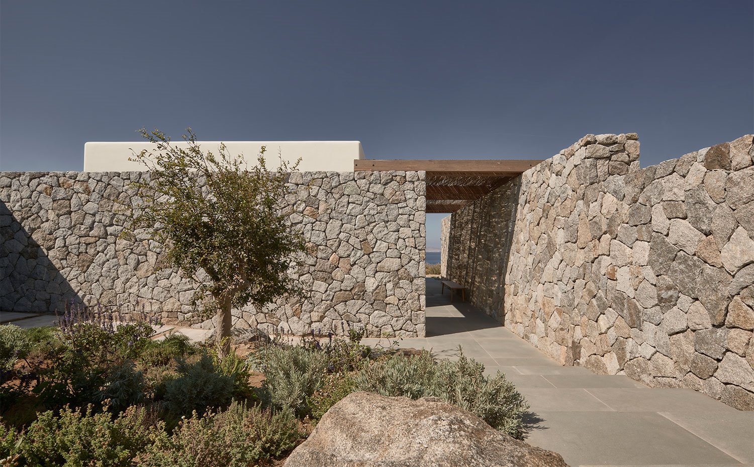 Zona exterior vivienda con paredes de piedra y vegetación autóctona