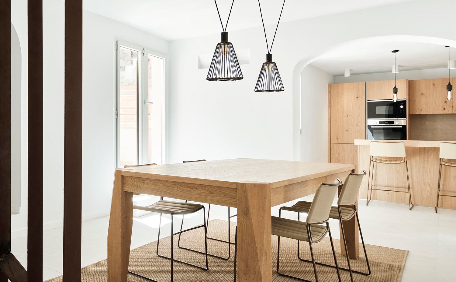 Comedor con mesa de madera y alfombra de fibras natural junto a cocina abierta