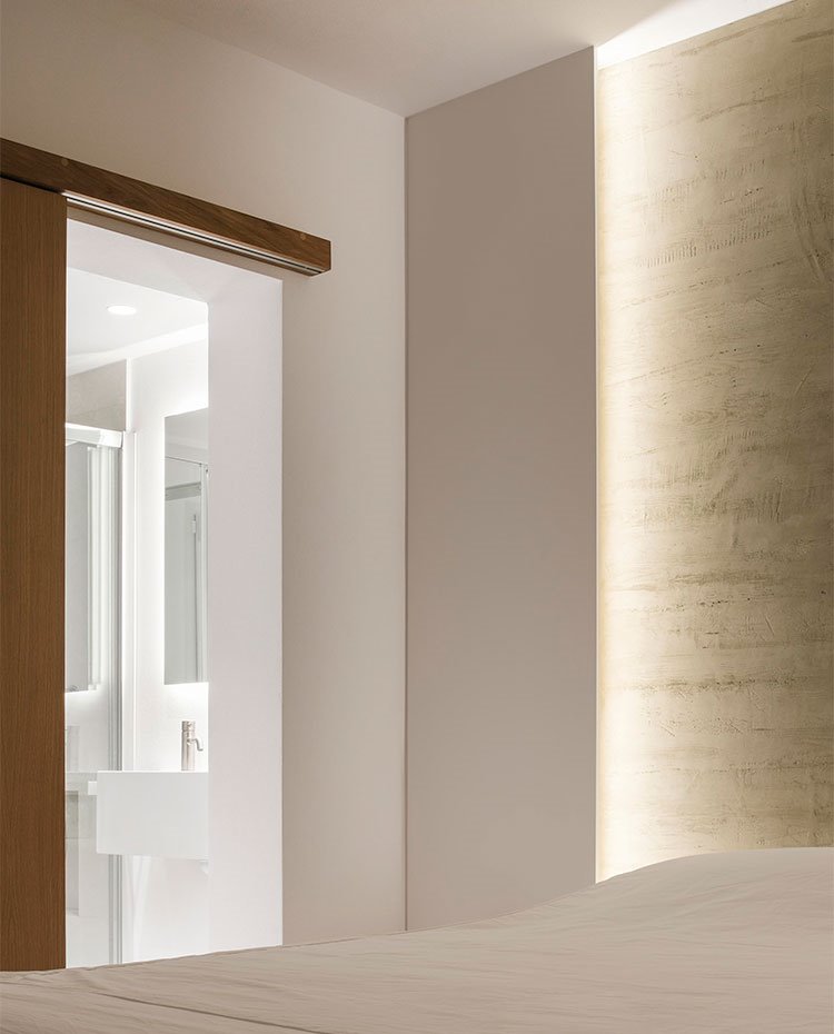 Dormitorio con iluminación indirecta en zona de cabecero y puerta corredera hacia baño