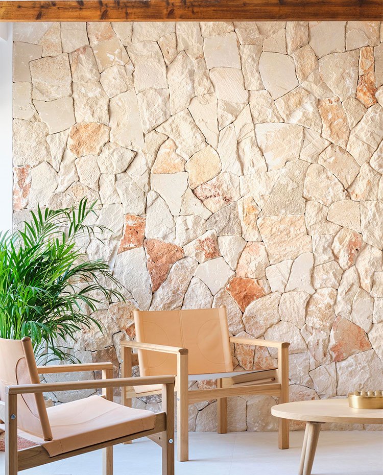 Pared revestida de piedra, butacas de piel y madera, y mesa de madera