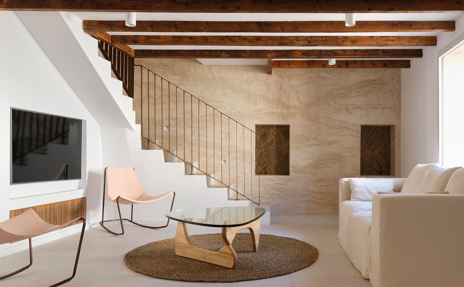 Salón con mobiliario de tonos claros, mesa de centro con sobre de madera y vigas de madera en el techo