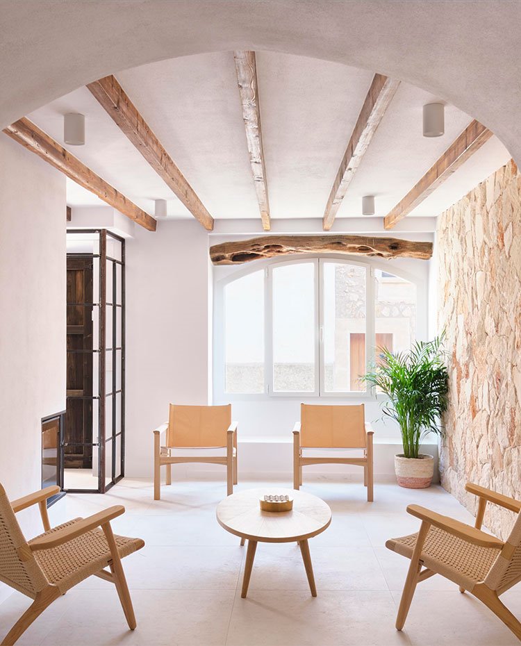 Zona de estar con butacas de piel y mesa de madera, techo con vigas de madera y zonas de paso abovedadas