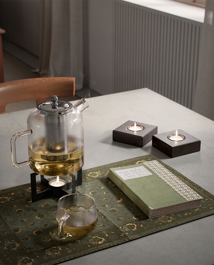 Tetera con taza, velas y un libro sobre la mesa