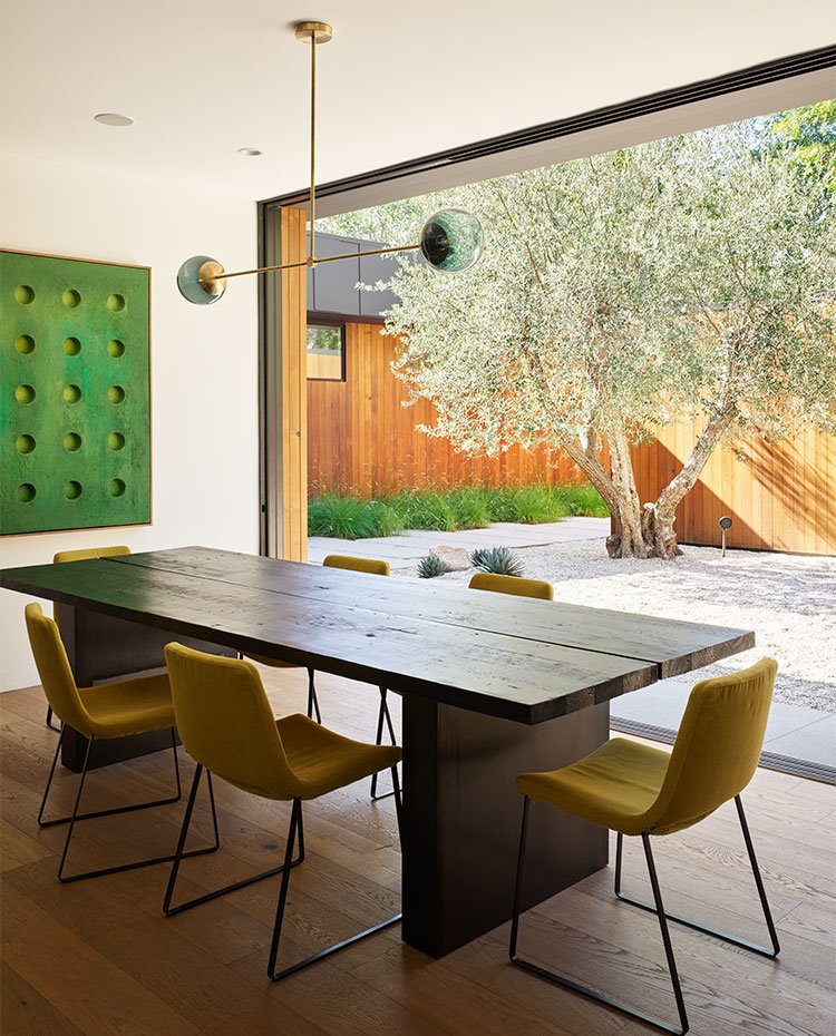 Comedor con mesa de centro de madera, sillas en color pistacho, luminaria suspendida, con gran apertura hacia exterior, suelo de madera