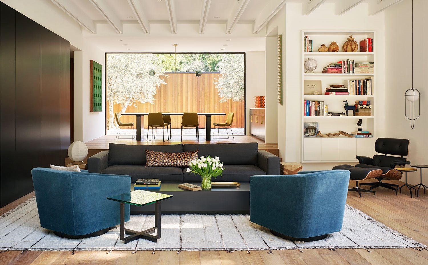 Salón con butacas tapizadas en azul oscuro, sofá y mesa en tonos oscuros sobre alfombra de tonos curdos