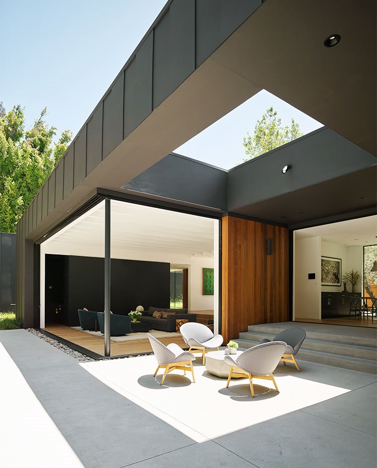 Zona de estar exterior con amplio lucernario en la estrucutra, junto a salón interior, pavimento de hormigón y mobiliario en color gris