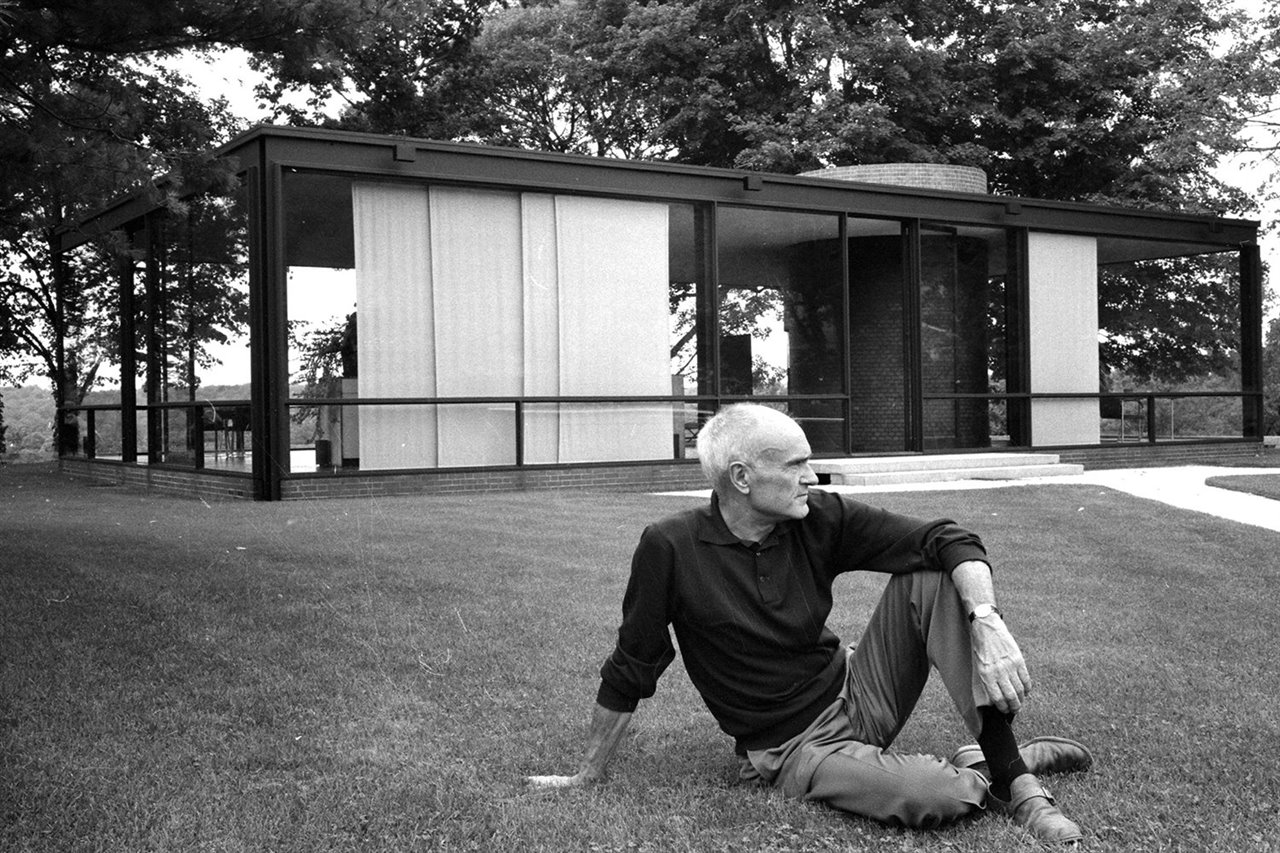 Philip Johnson retratado frente a la Glass House, su obra más conocida y emblemática.