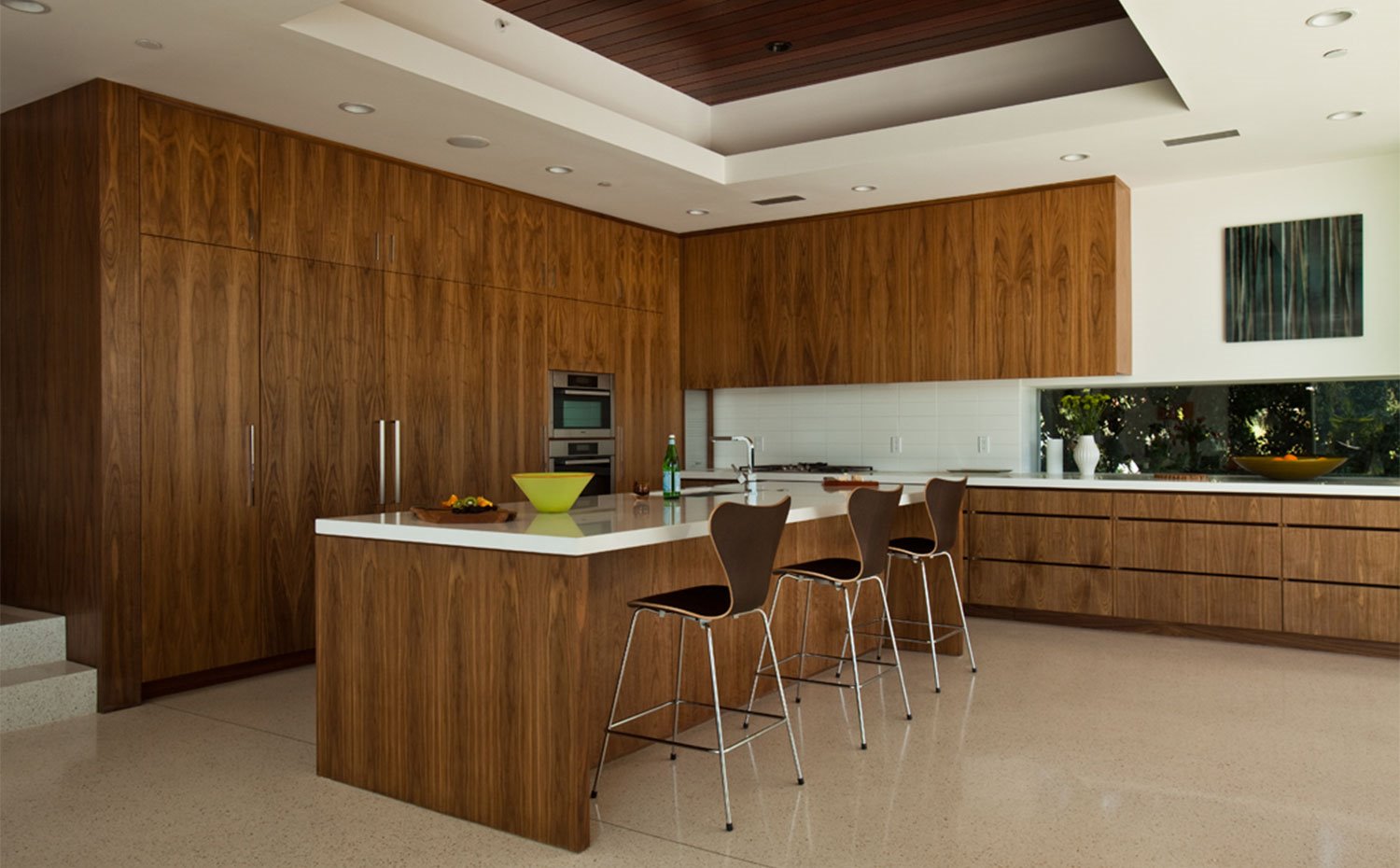 Amplia cocina con isla central, encimera en crudo en contraste con mobiliario en madera, taburetes altos en a juego con el mobiliario