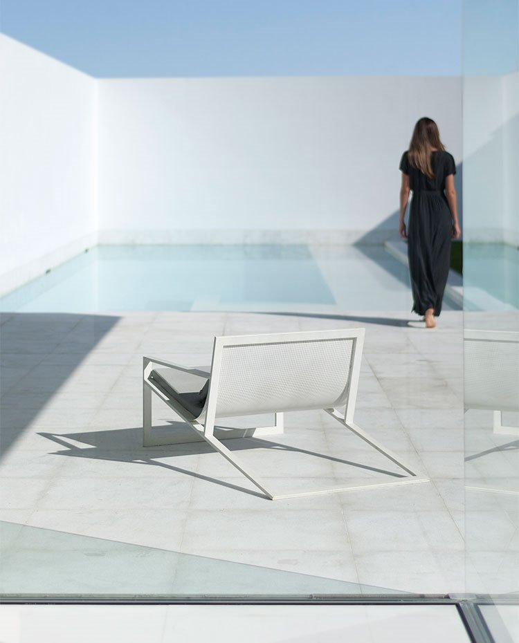 Butaca exterior junto a piscina, delimitado por un alto cerramiento en blanco