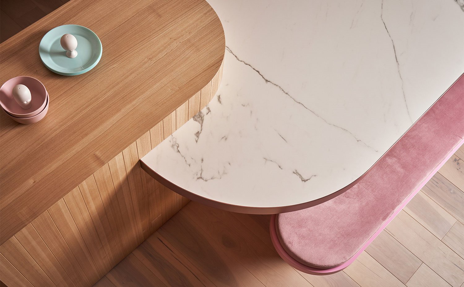Detalle mesa de comedor con encimera de mármol blanco jutno a estructura en madera y asientos en rosa 