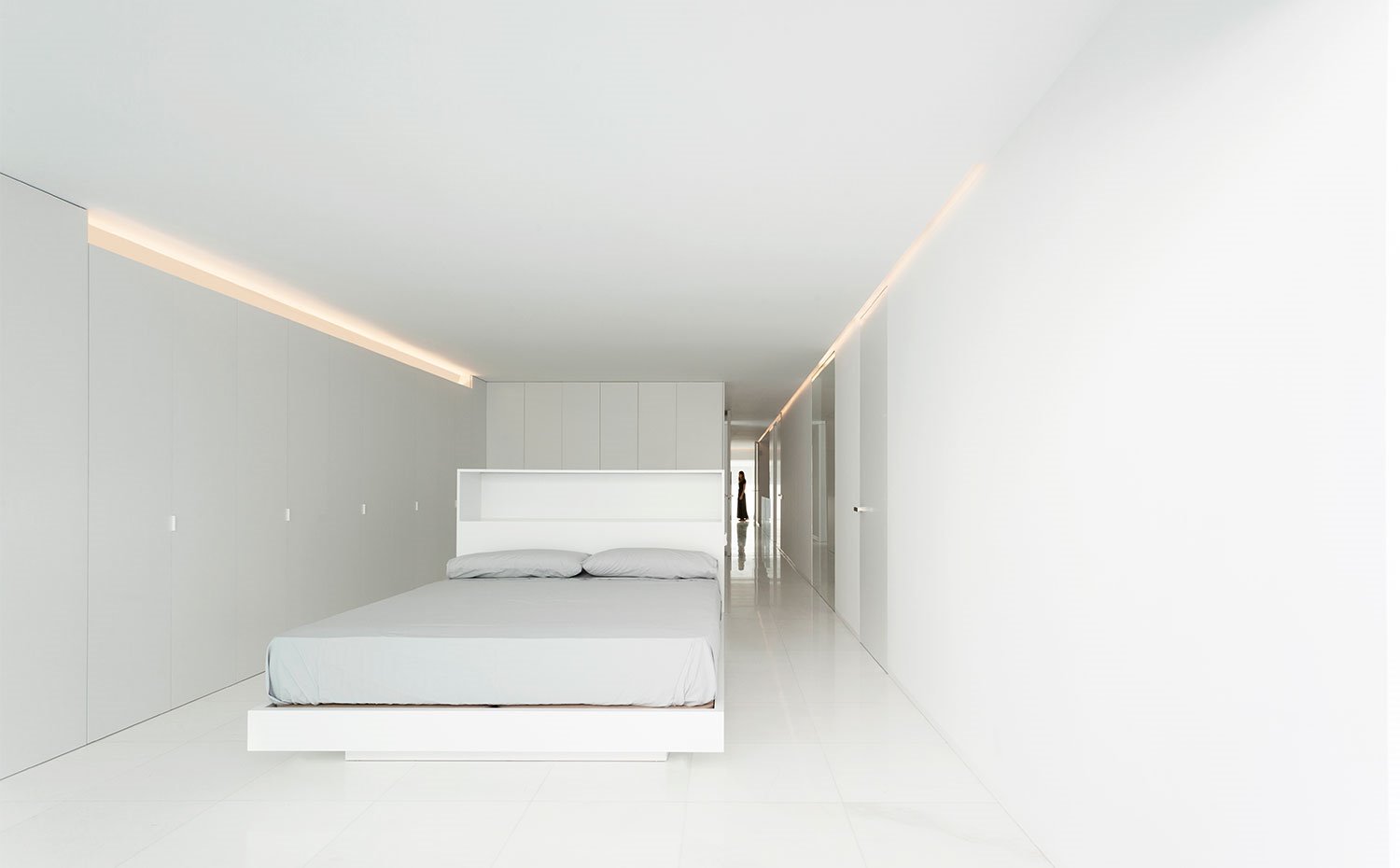 Dormitorio de gran profundidad con frente de armarios en blanco y estructura de cama a juego