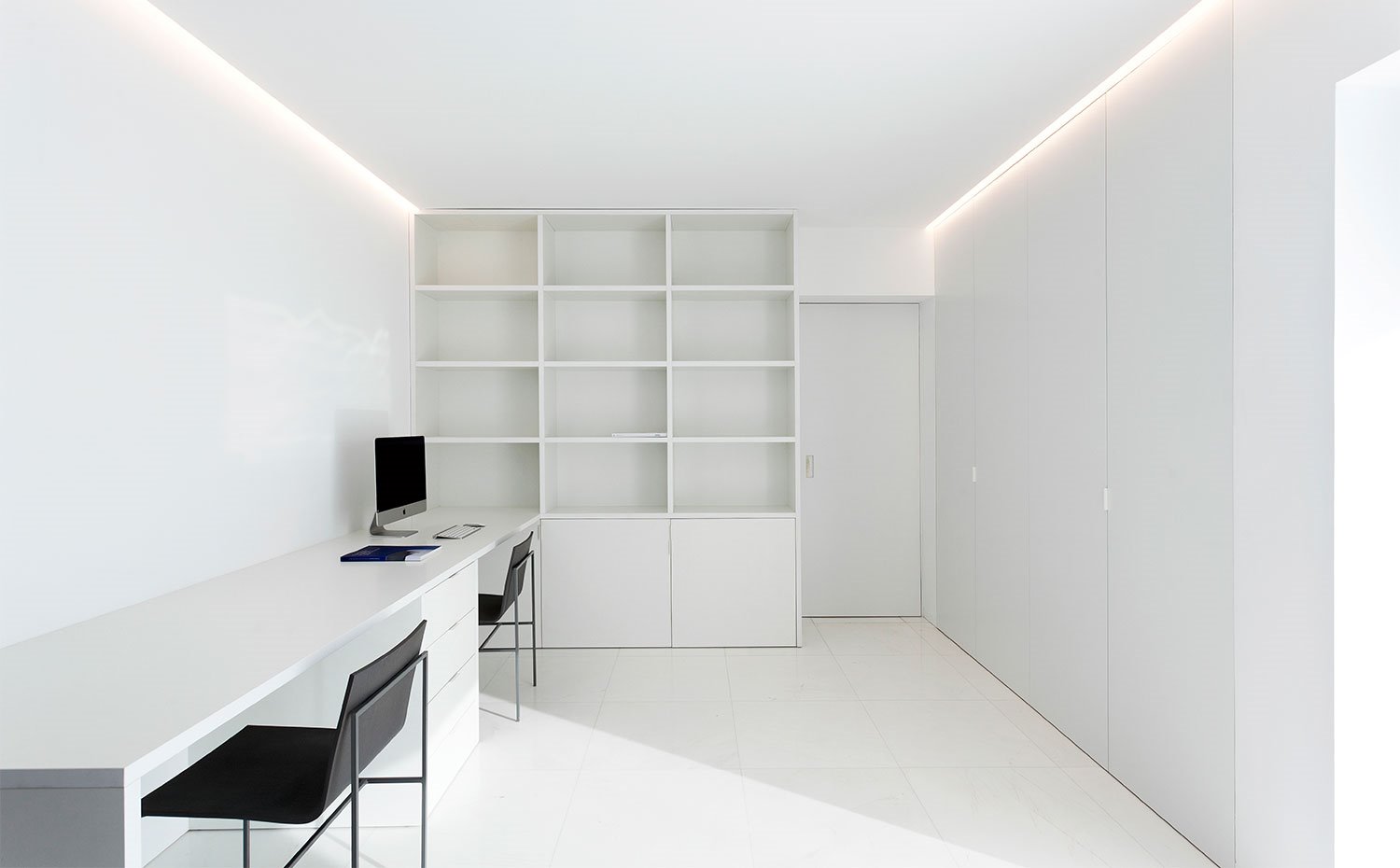 Habitación a modo estudio con mesa de trabajo y librería hecha a medida, en blanco, en contraste con sillas en negro