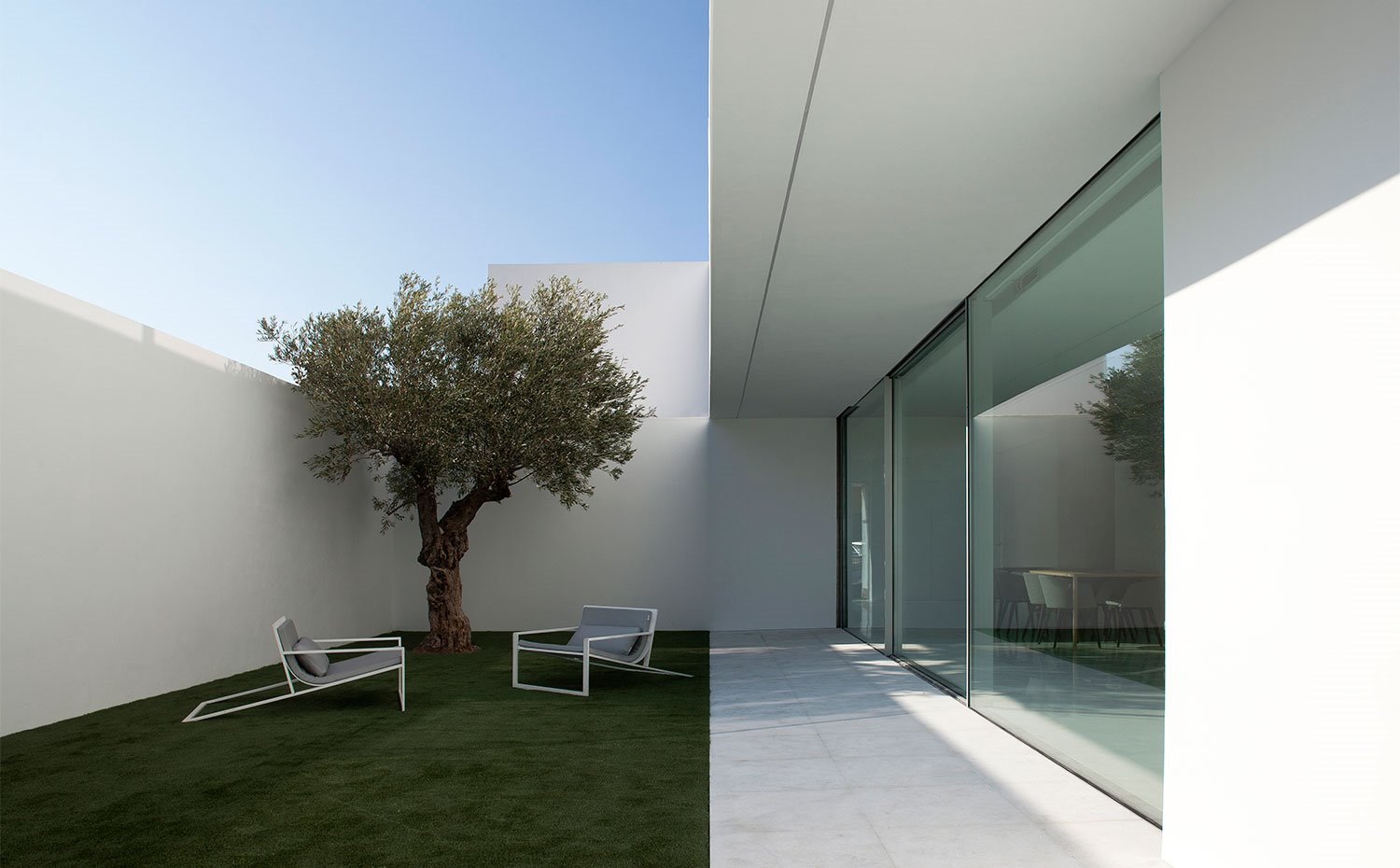 Rincón de terraza junto a sombra de árbol y con cerramientos de cristal hacia el interior