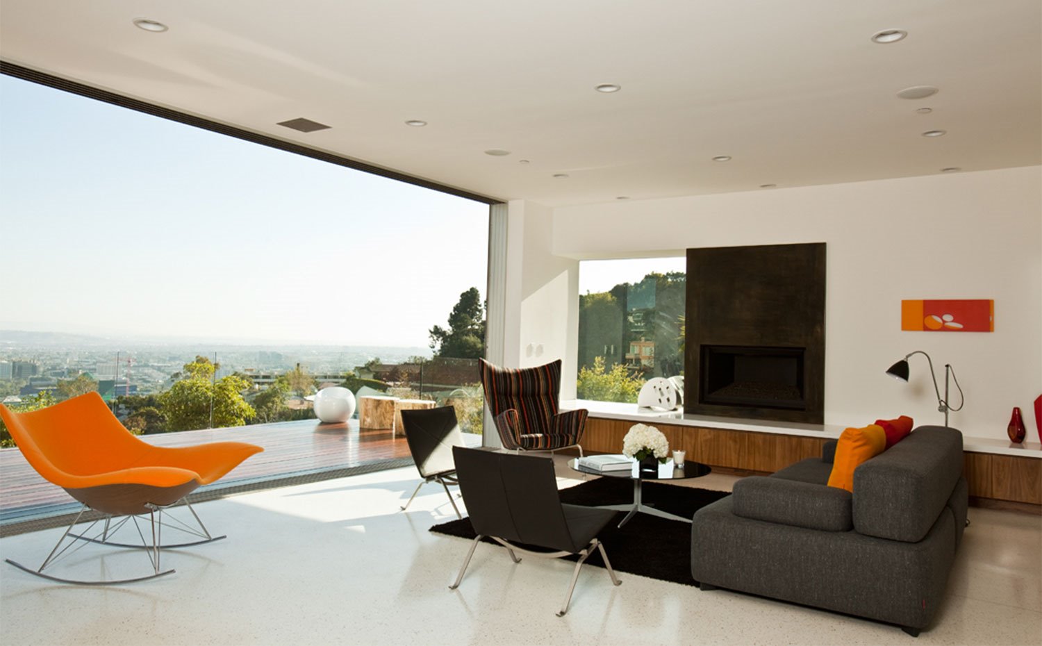 Sala de estar con apertura total hacia exterior, mobiliario en tonos grises, negros y toques en naranja