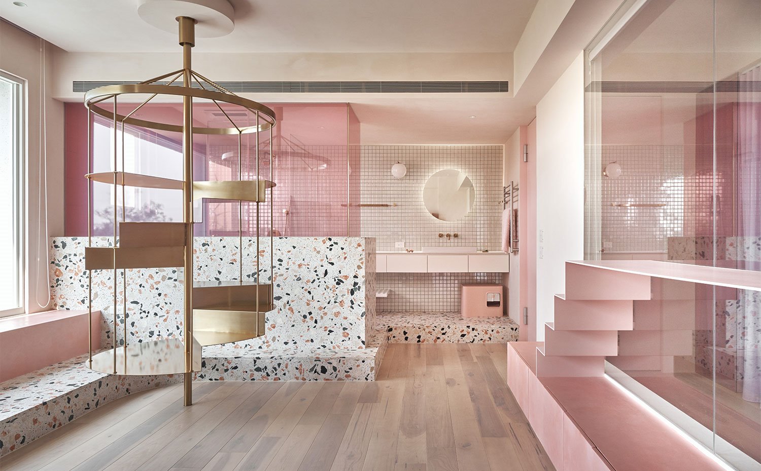 Vista general de zona de estar con cuarto de baño al fondo, detalles en rosa y suelo de madera
