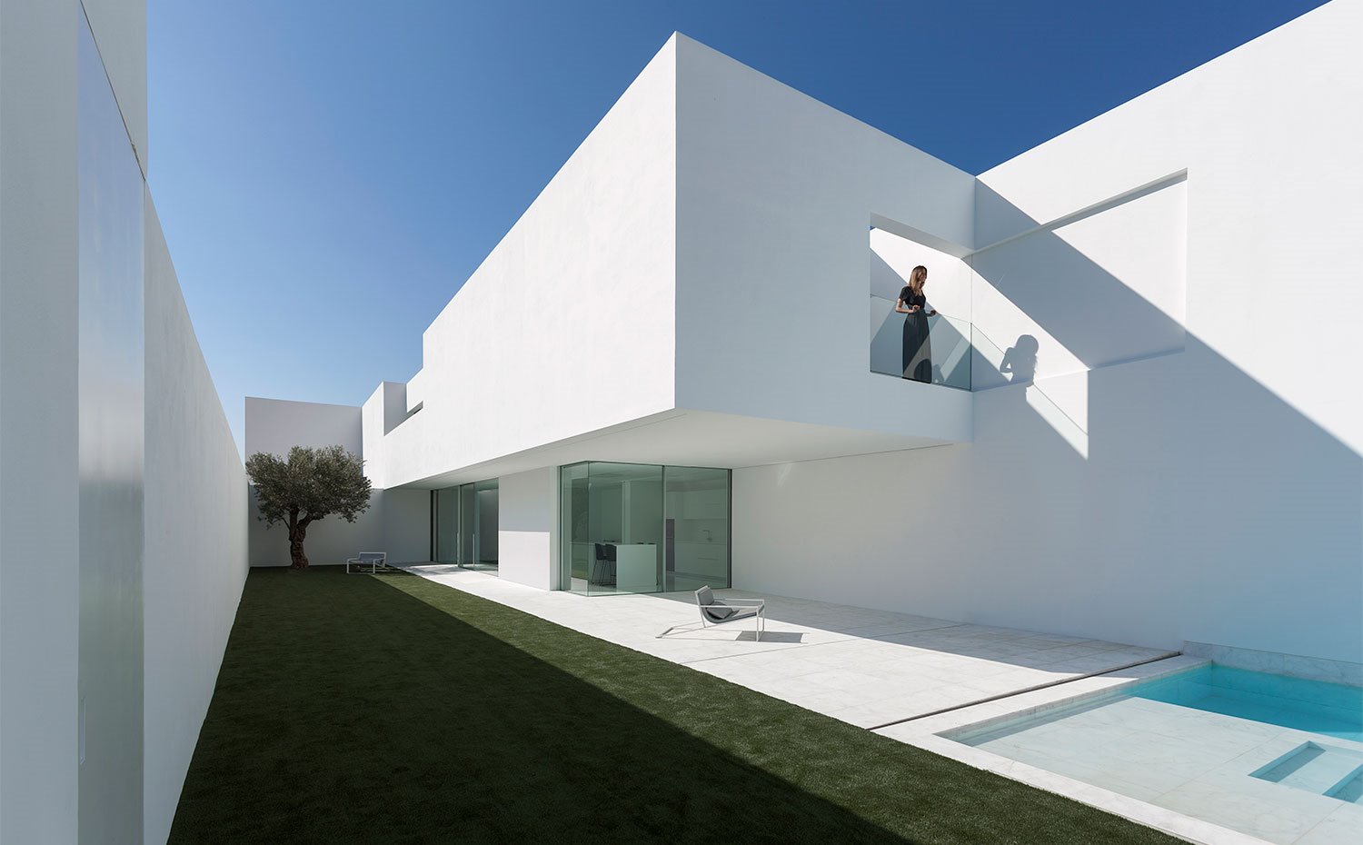 Vista general del exterior de la vivienda, totalmente en blanco, que contrasta con el verdor del césped y el azul del cielo
