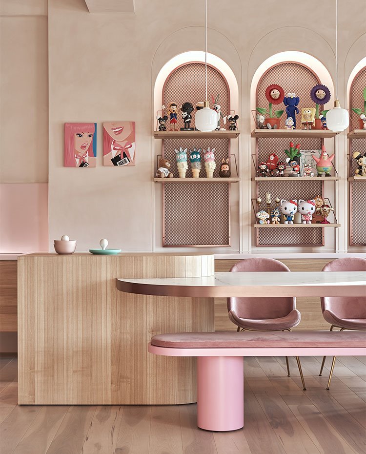 Zona de comedor con asientos en rosa, estructura en madera y estanterías decoradas con figuras de anime y dibujos animados