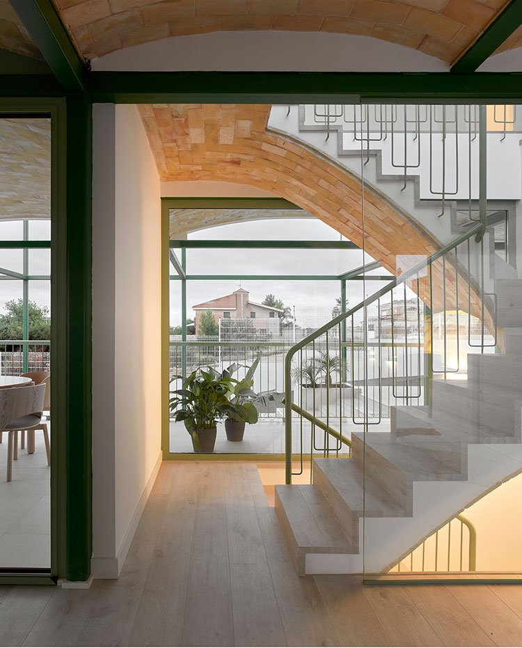 Detalle de escaleras con peldaños revestidos de madera, barandilla en verde y techo abovedado