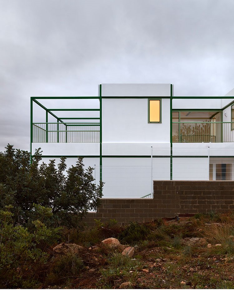 Exterior de vivienda con fachada en hormigón pintada en blanco y aperturas con cerramientos de cristal y perfil metálico