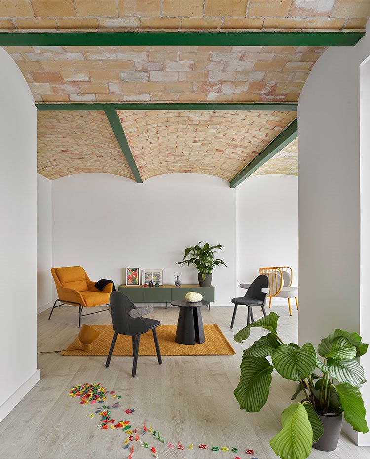 Interior de salón con mobiliario de estilo escandinavo, alfombra y butaca en tonos mostaza, consola en verde y sillas y mesa en gris