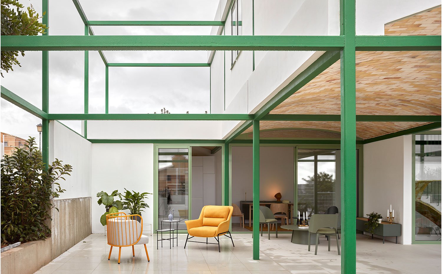 Terraza con zona cubierta y descubierta, con mobiliario de estilo nórdico, estructura metálica en verde y hormigón pintado en blanco
