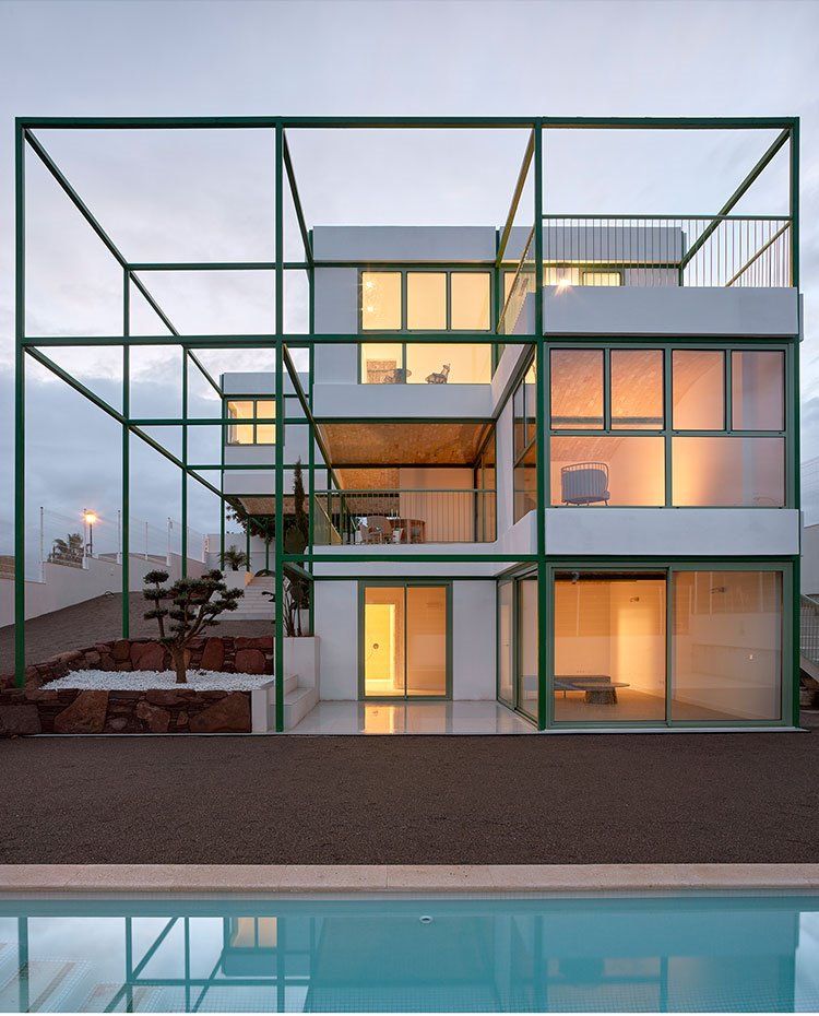 Vista al anochecer de la vivienda con iluminación tenue en el interior y piscina en la parte frontal