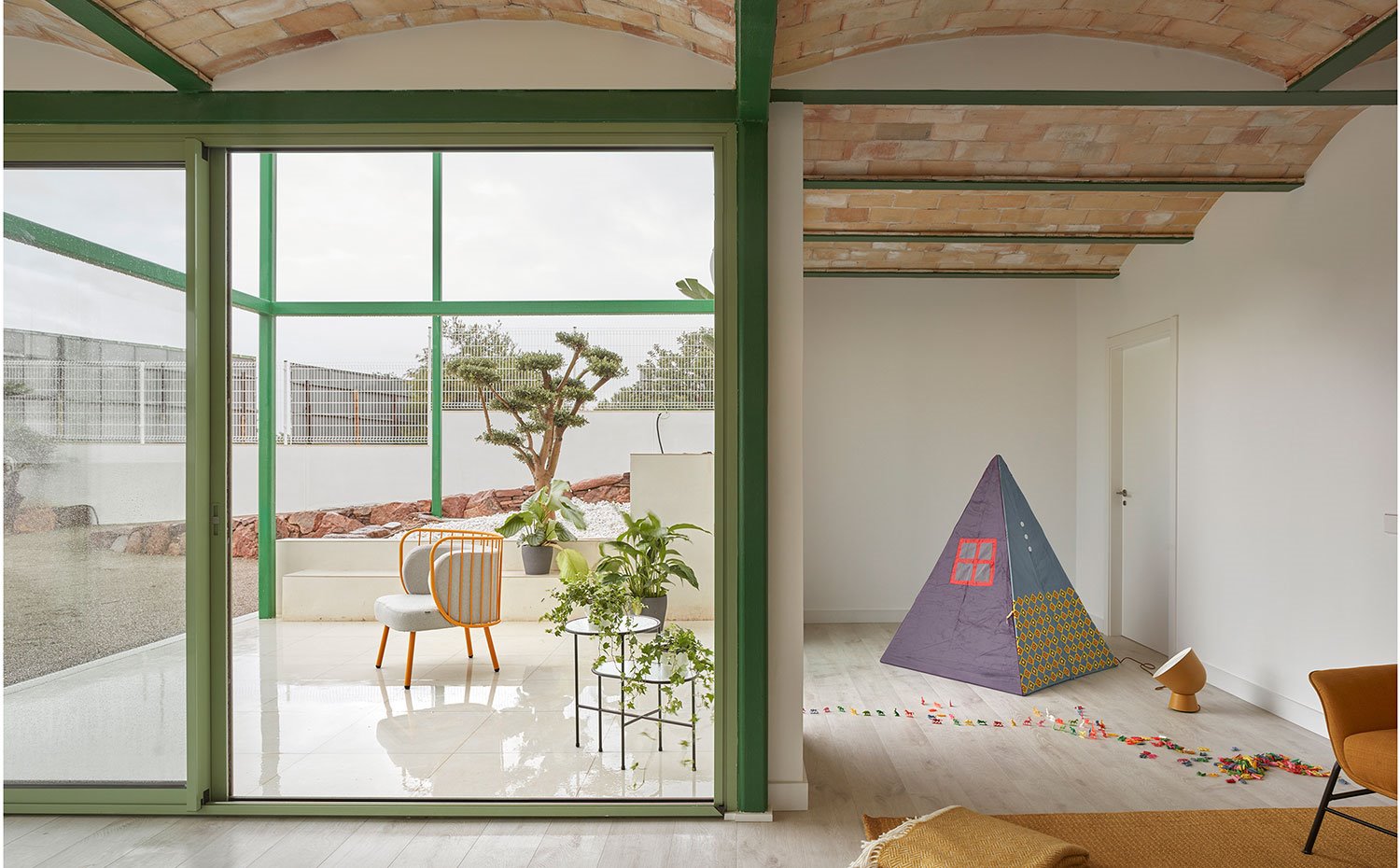 Zona de estar con rincón para juegos infantiles con un tipi, luminaria en color mostaza, cubierta en bóveda