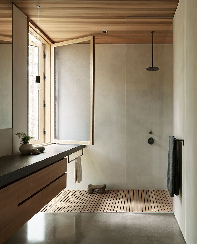Cuarto de baño con encimera de granito negro y módulo bajolavabo suspendido de madera, ducha tras hoja de cristal transparente y pie de ducha con listones de madera