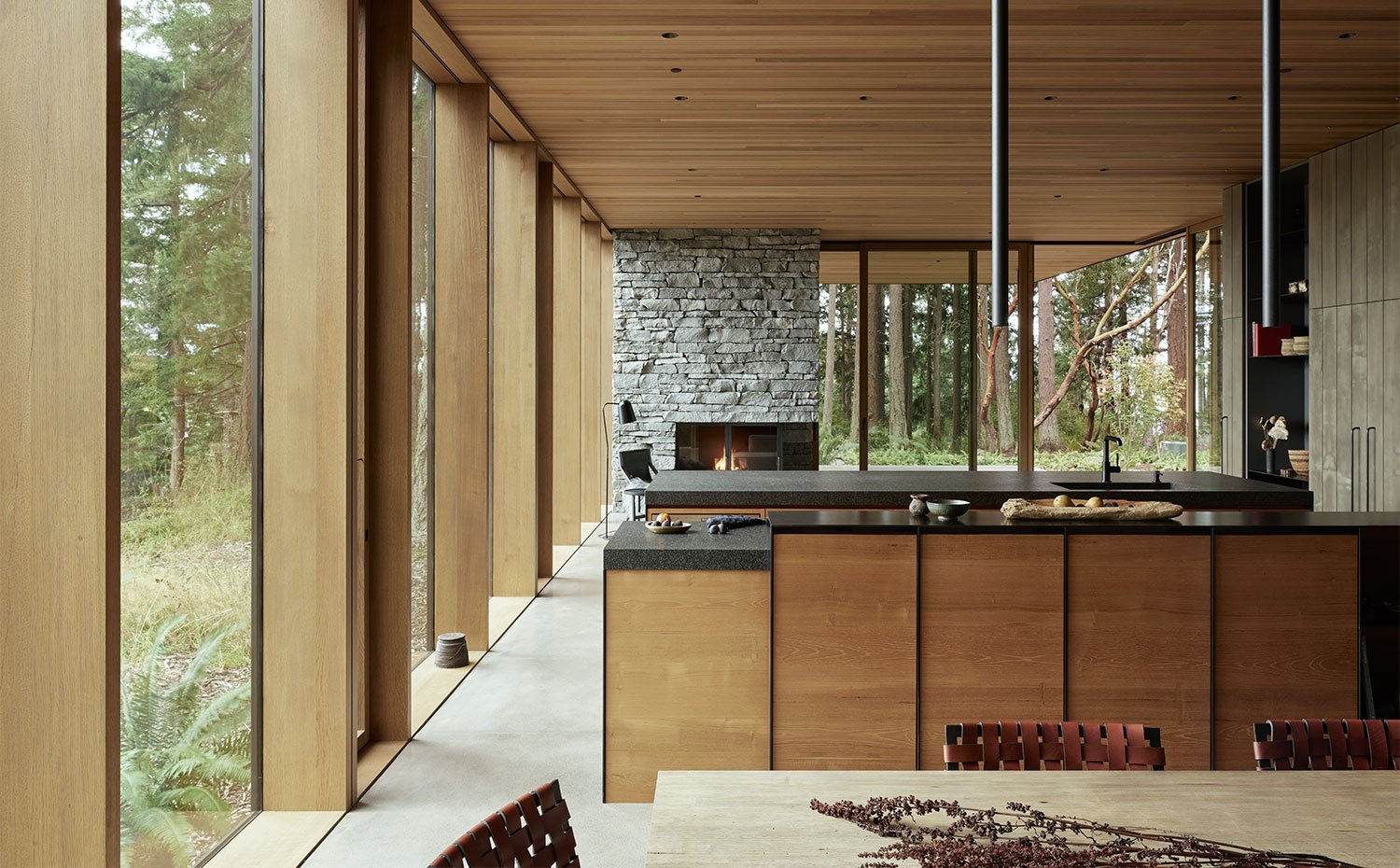 Mobiliario de cocina en acabado madera y encimera en granito negro, luminarias suspendidas cilíndricas, con doble isla de trabajo