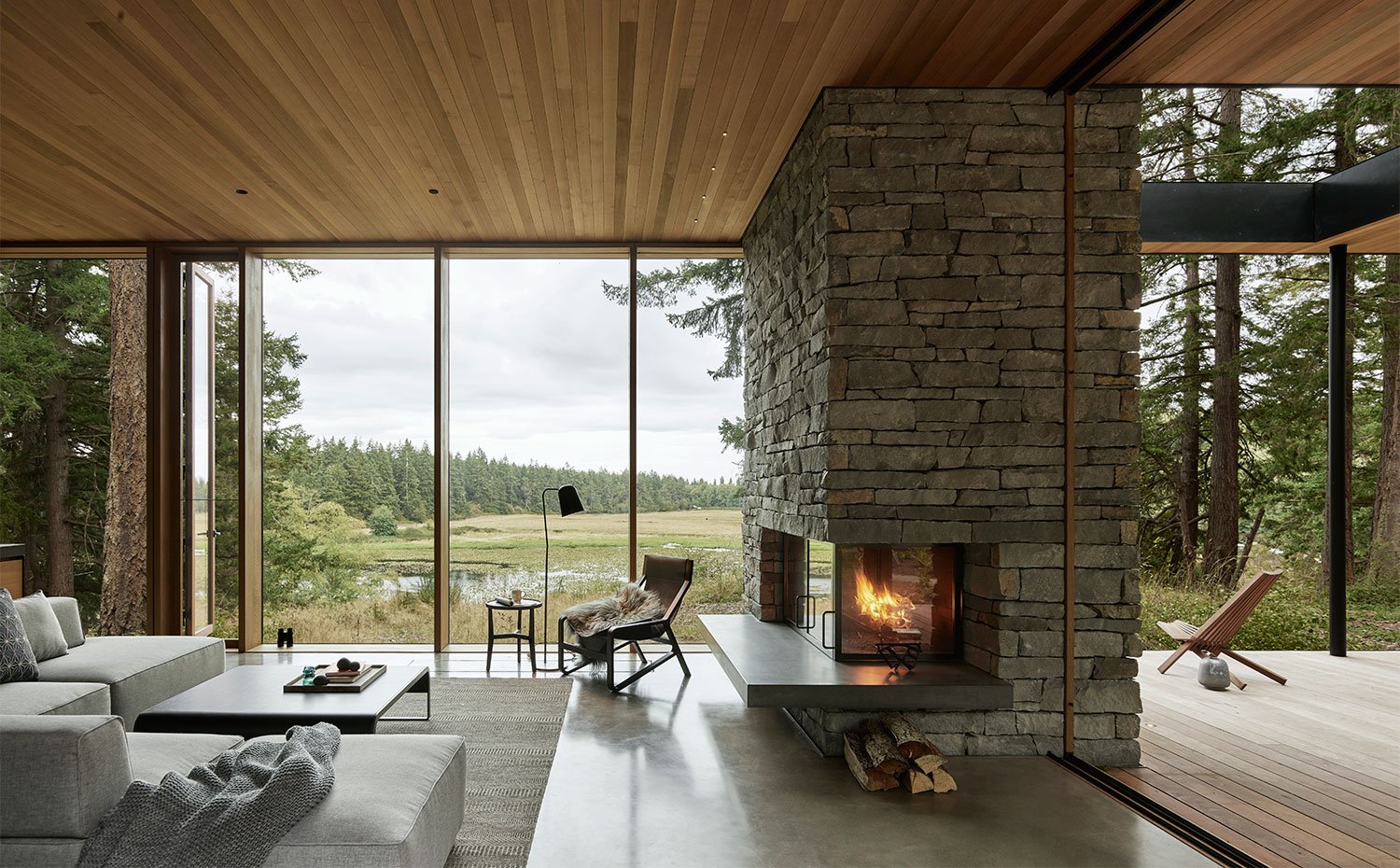 Salón con chimenea de piedra vista, cerramiento corredero acristalado hacia terraza cubierta exterior