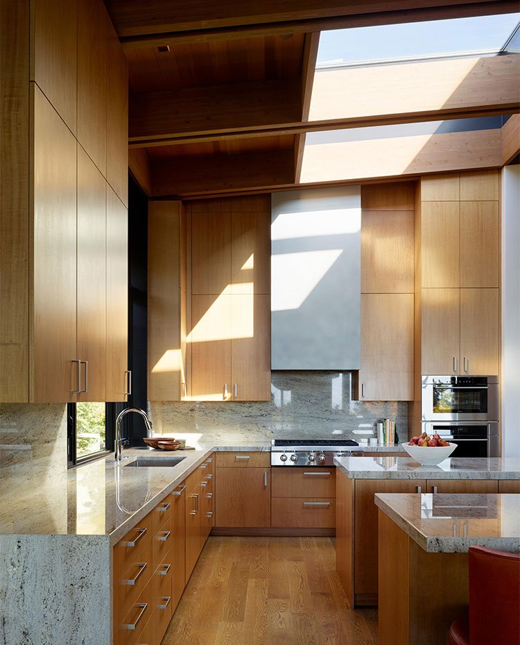 Cocina con mobiliaario de madera y encimera de mármol, grandes lucernarios en el techo