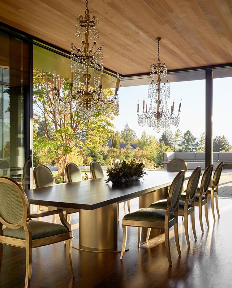 Comedor formal con larga mesa y sillas de estilo clásico, dos lámparas de araña cuelgan del techo