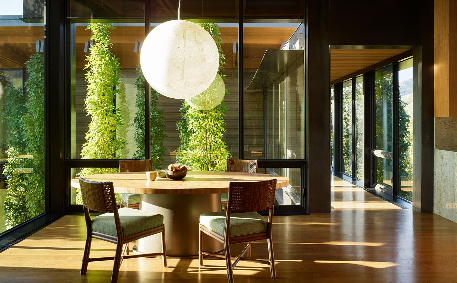 Mesa de comedor circular junto a sillas de madera y asientos tapizados, rodeados de cerramientos de cristal