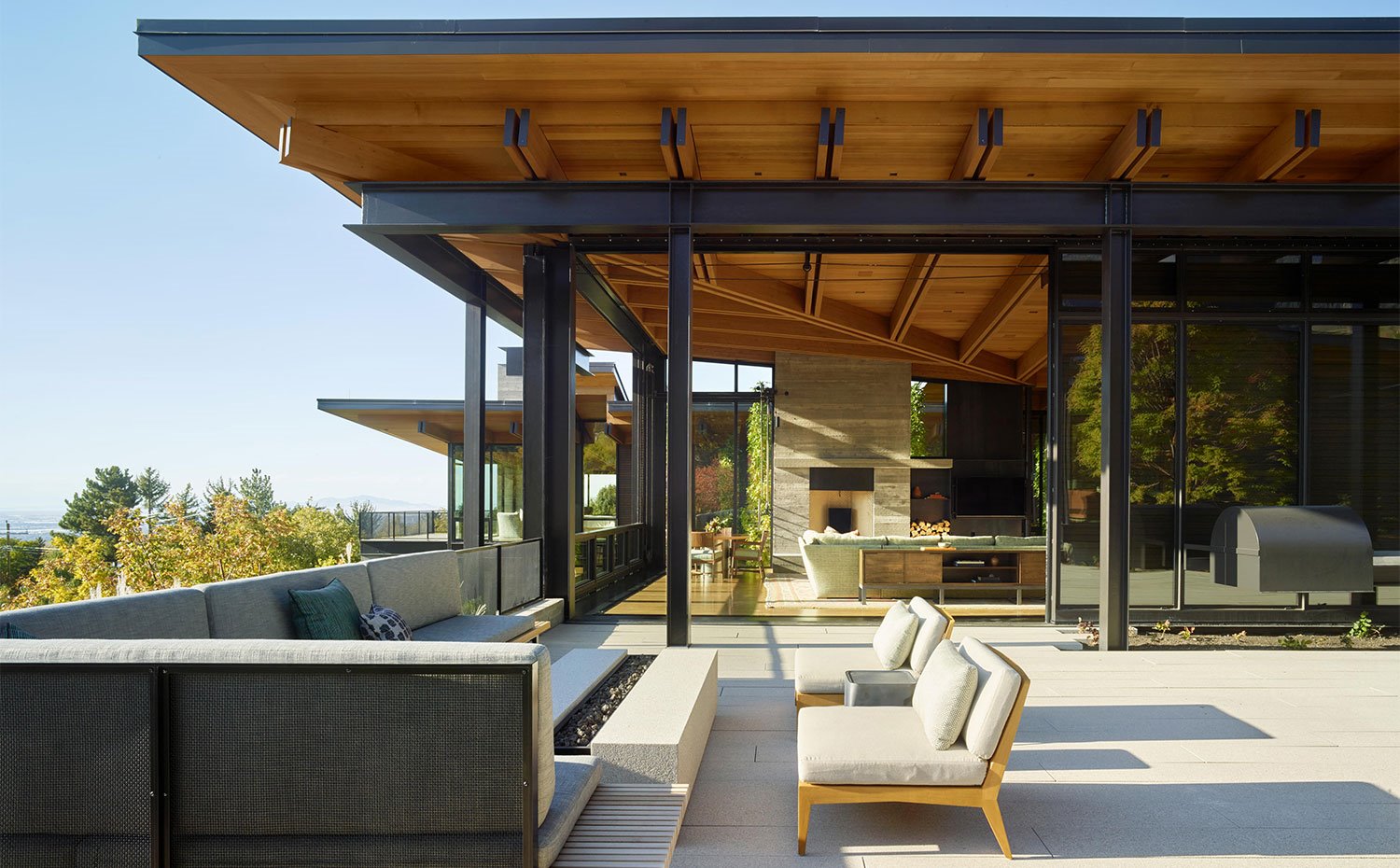 Terraza exterior junto a salón, con bancada y butacas alrededor de una fuego