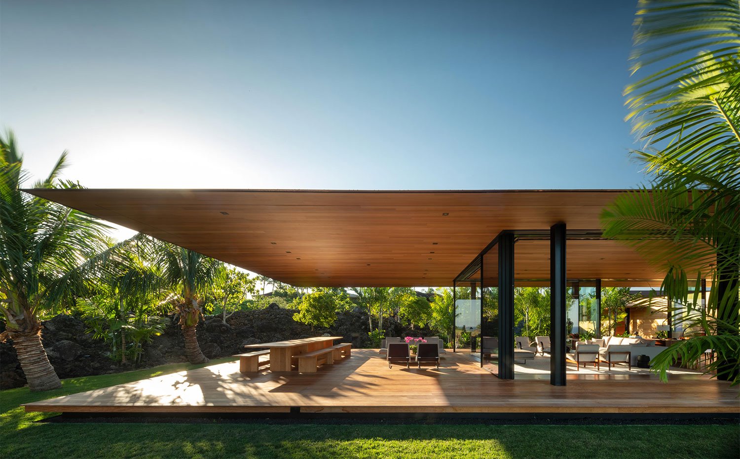 Comedor y salón exterior en terraza cubierta rodada de palmeras y zona ajardinada