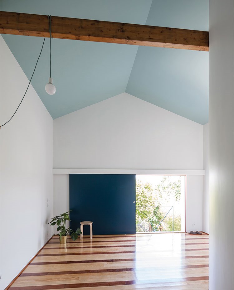Dormitorio con amplio cerramiento corredero en azul cobalto, techo a dos aguas en azul claro, suelos de madera