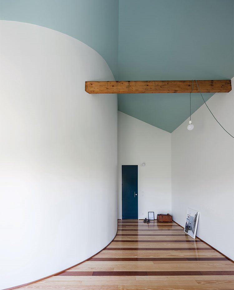 Dormitorio con pared curva, viga de madera en techo con luminaria suspendida congando de viga