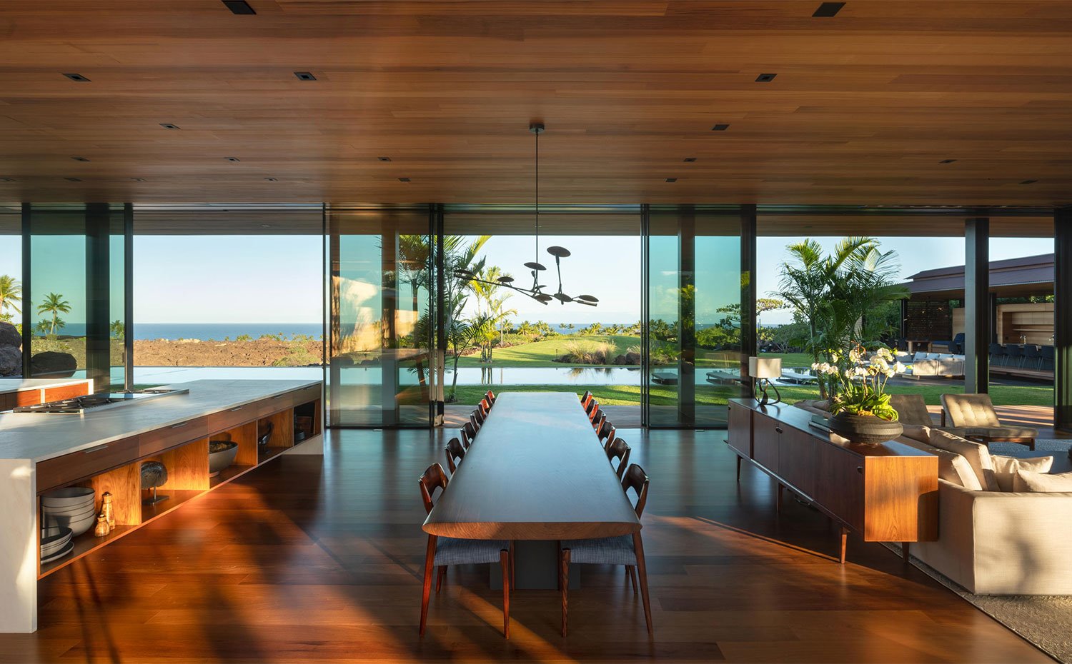 Gran mesa de comedore en madera con módulos abiertos de cocina y consola tras la que dispone el salón