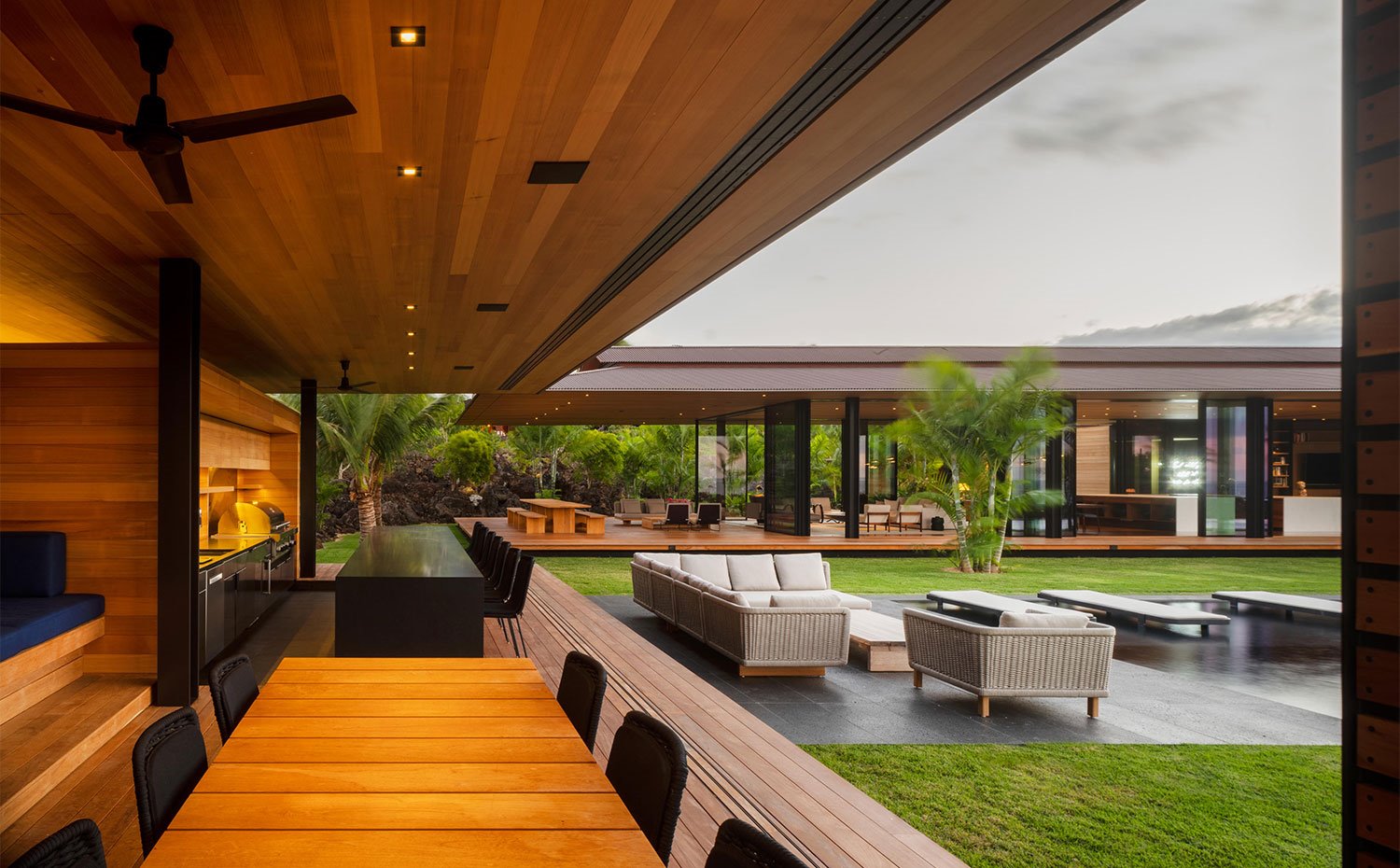 Módulo con cocina abierta con isla, mesa y bancada de madera dispuestas frente a una zona de estar exterior