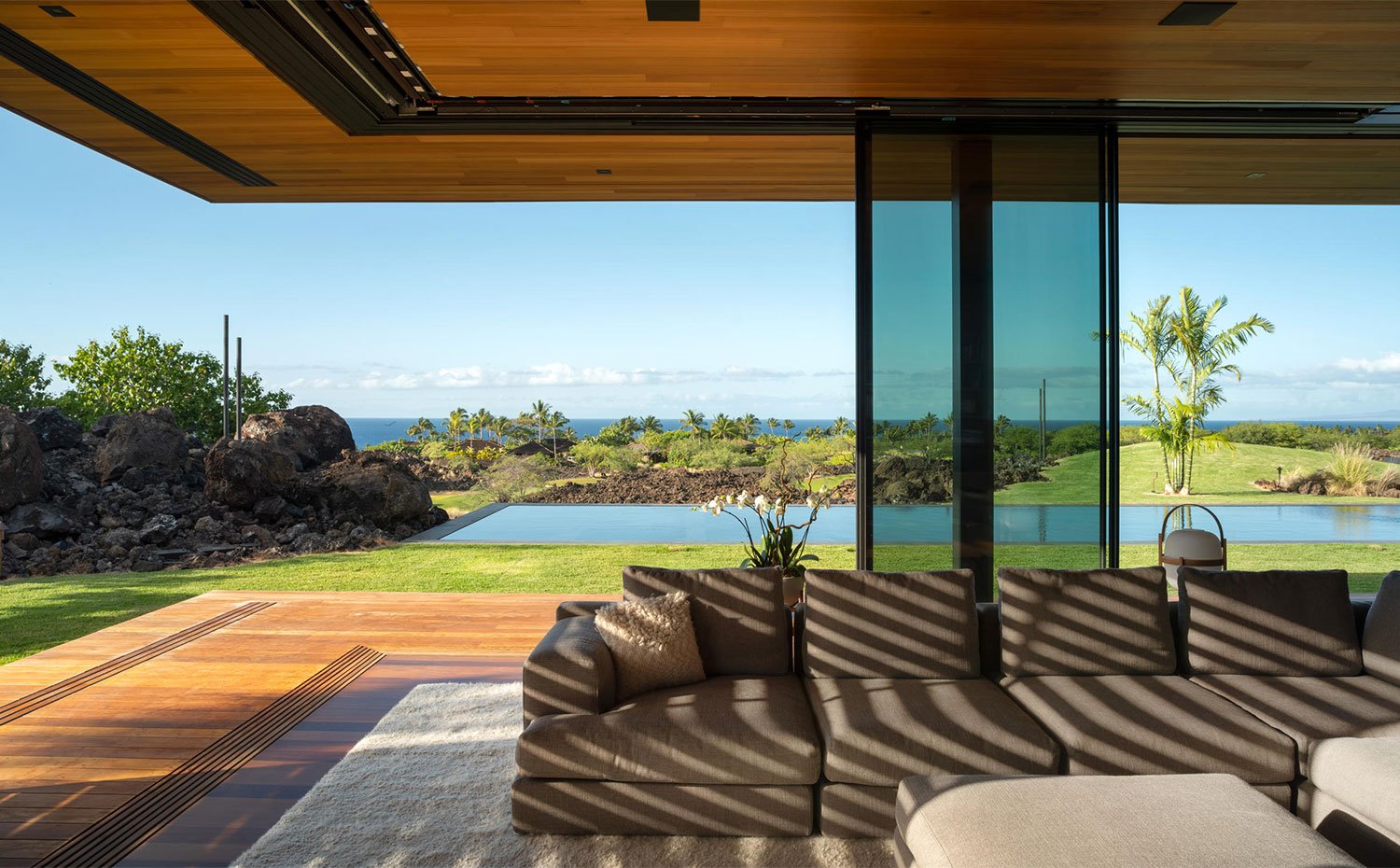Sofá en gris sobre alfombra en color crudo de salón que se abre al exterior, junto a piscina y vistas al mar