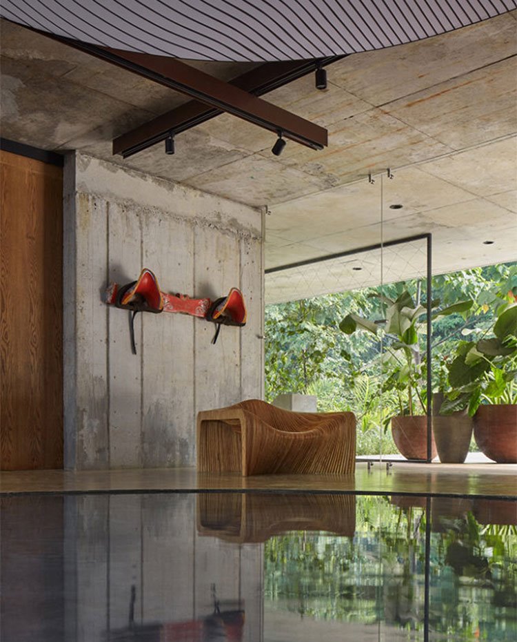 Butaca de formas orgánicas de madera, colgadores en pared de color rojo y paredes de hormigón visto