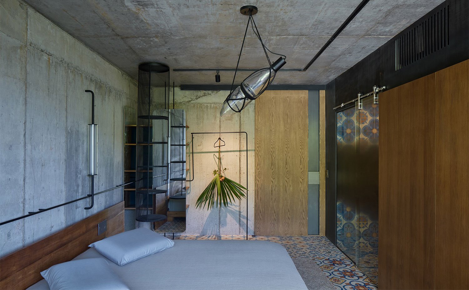 Dormitorio con pared y techo de hormigón, baldosas hidráulicas en el pavimento y armarios y cerramientos en madera, cristal y estantes metalizados