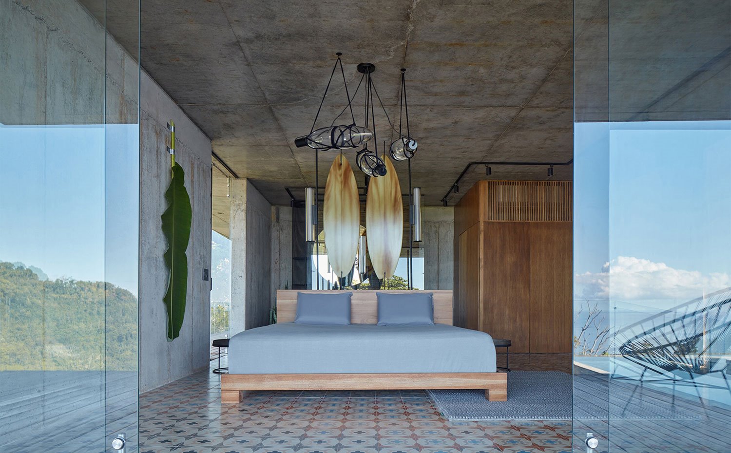 Dormitorio principal con cama y armario de madera, suelo de baldosas y cerramientos correderos hacia exterior en cristal transparente